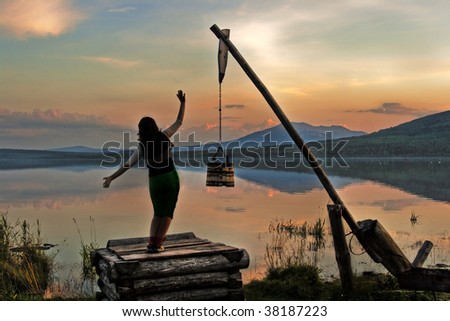 Decline on mountain lake. Silhouette of the girl. Old well. Reflection of the sky in water