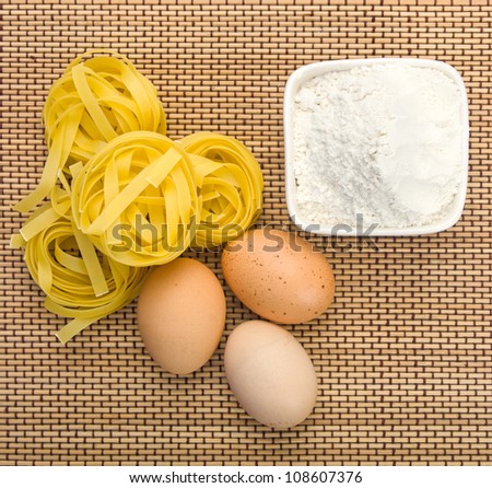 Pasta, eggs and flour on straw background