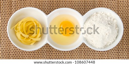 Pasta, egg yolk and flour on straw background