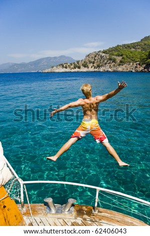 Young man on vacation jumping from a boat in turkey, enjoying his freedom, while on a summer holiday