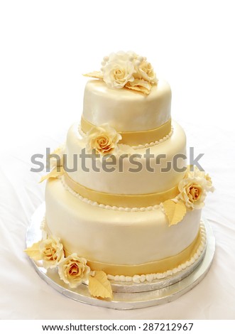 Wedding cake, on white (not isolated) background. 3-tiers covered in ivory fondant sprayed with pearl spray and yellow/gold roses made of sugar paste.