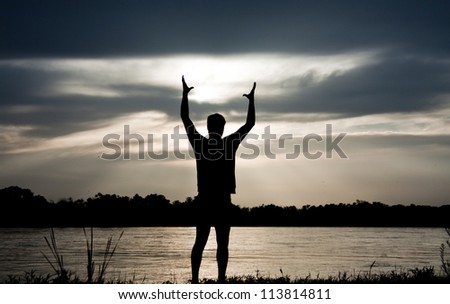 Silhouette of man on the river, holding his hands up, hugging the sun