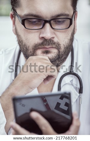 Doctor with stethoscope around his neck looking at the tablet PC