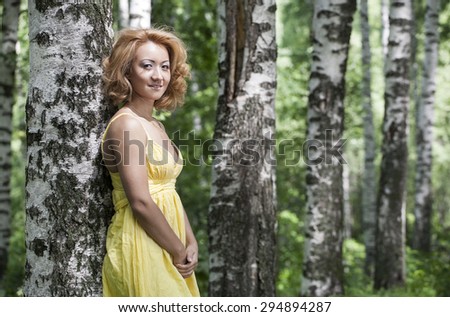 portrait of beautiful woman in yellow blouse standing and smiling at birch forest