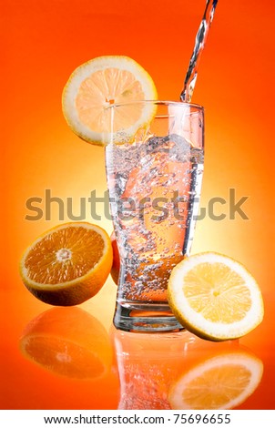 Pouring of mineral water in glass with a lemon and orange on a Orange background