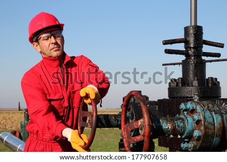 Oil and Gas Well Drilling Worker. Oil industry. Worker turning valve on oil well pump jack.