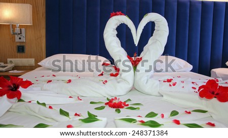 Towels arranged as swans on the bed in hotel room. Romantic Flower Petal Arrangement on a Hotel Bed. Honeymoon bed decorated with red petals and towels. Swans Made from Towels Surround by Red Petals.