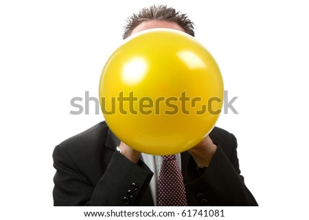 A mid thirties business man blowing up a yellow balloon.  Facing camera.   Studio isolated on a white background.