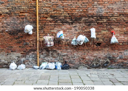 Venice, Italy - March 12, 2011: Old red Brick wall with with plastic trash bags hanging on nails.