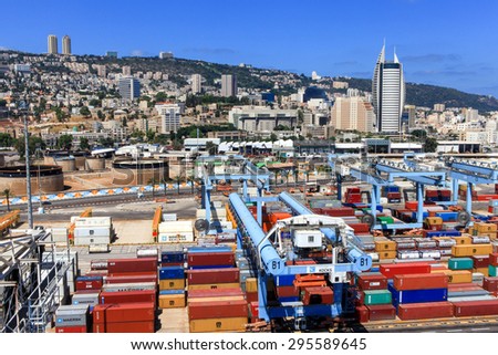 Haifa, Israel - July 10, 2015: Various brands and colors of shipping containers stacked in a holding platform waiting for loading with the city of Haifa in the background