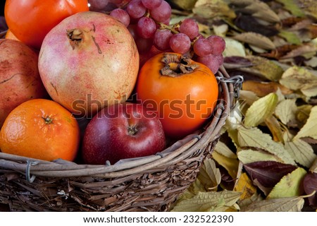 Old basket fruit bowl with autumn fruits isolated over black background. Surface full of dry leaves