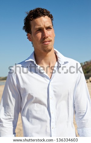 Young handsome man with a goatee, a tan and wet curly hair wearing a white shirt looking worried. Mediterranean type.