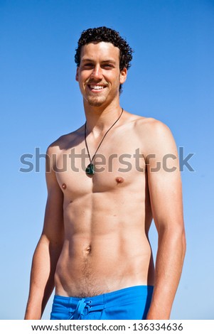 Young handsome muscular man in a bathing suit hanging on the beach. Surfer type.