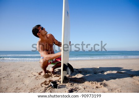 Surfer checking his surf board on the sand.
