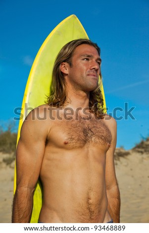 Fit long haired blonde surfer standing in front of his surfboard.