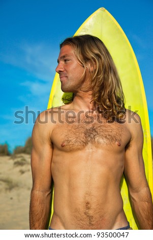 Fit long haired blonde surfer smiling in front of his surfboard.