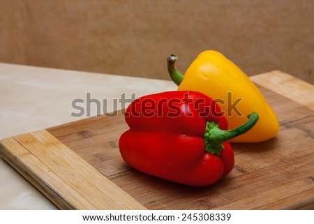 Two peppers on a board. One red and one yellow