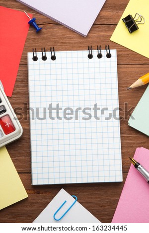 checked notepad and office accessories on wood background