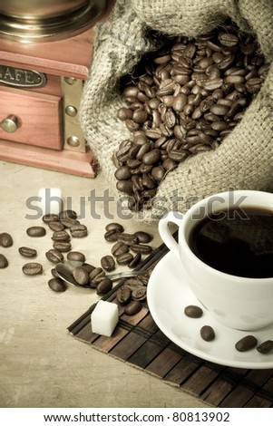 cup of coffee and grinder with roasted beans on wooden background