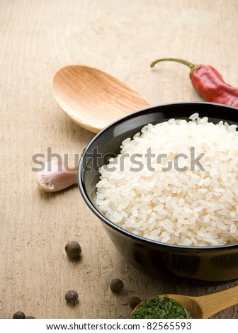 uncooked rice in bowl with spoon on wood background