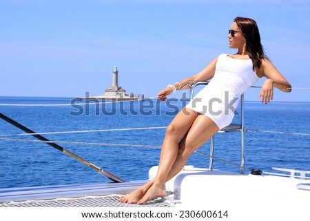 woman lies on a luxury catamaran yacht in the sea and looking to the horizon with lighthouse and blue sea in background
