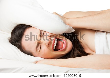A frustrated tired woman hides her head in her pillow and screams because she can\'t sleep. Isolated on white.