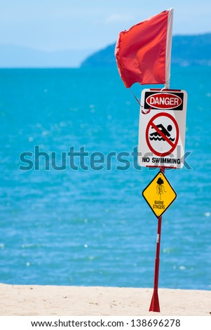 Close-up of a jellyfish or marine stinger warning sign and red flag at a tropical Australian beach.