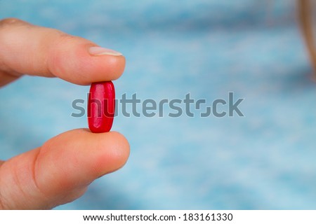 Close-up shot of fingers holding a red pill.