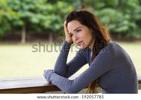 A sad and depressed woman sitting down alone outdoors