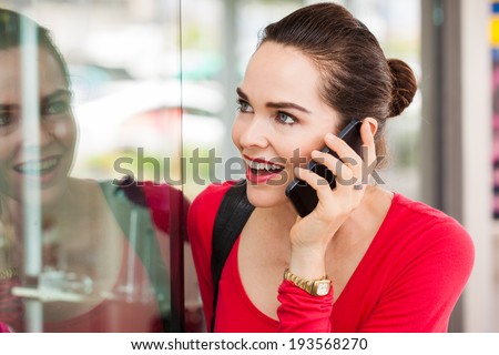 A beautiful happy woman is talking on the phone and looking in a shop window.