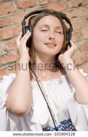 Girl Music Fun or portrait of a beautiful young woman teen smiling with eyes closed listening to headphones on brick wall background