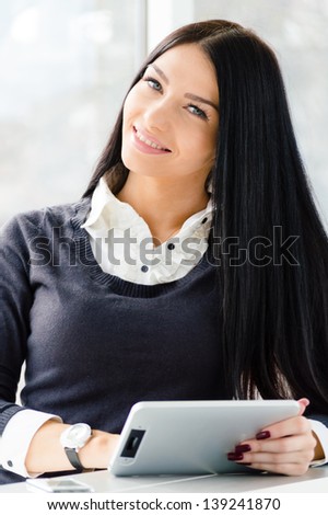 Portrait of a happy smiling young business woman using notebook PC relaxing near office window indoors