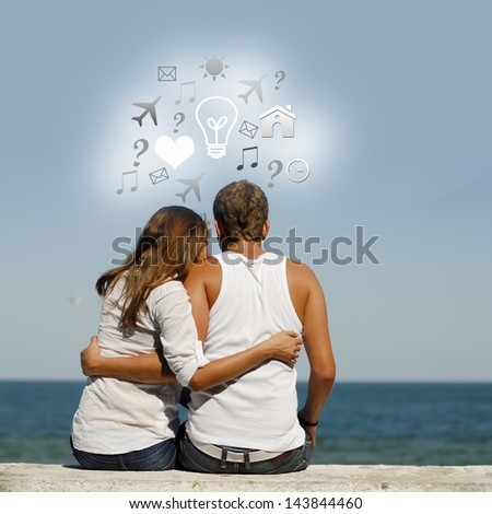 Young happy couple at sea coast sitting hugging with dialog box above them & blue summer sky and sea on the background
