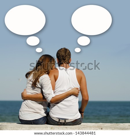 Young happy couple at sea coast sitting hugging dialog box above them & blue summer sky and sea on the background