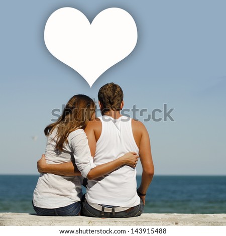 Young happy couple at sea coast sitting hugging heart dialogue box above them & blue summer sky on the background
