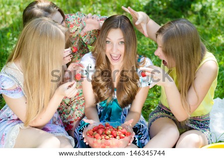 Four happy teenage girls eating strawberry and having fun outdoors on summer day