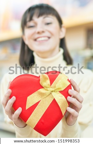 Happy young smiling beautiful woman holding red gift box in form of love heart