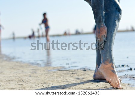 Mature woman applying mineral blue mud on legs at Sivash lake outdoors