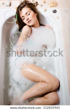 Portrait of young pretty woman sitting in bath with foam and soap bubbles