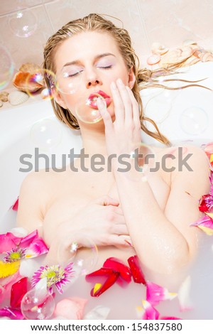 Beautiful sexy lady relaxing by taking a bath with flower petals