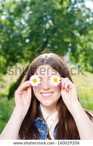 Funny teenage girl holding daisy flowers at her eyes on summer outdoors background