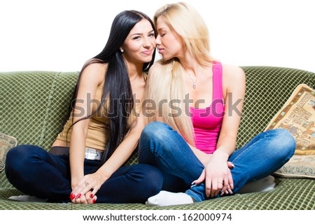 Portrait of two beautiful girlfriends or sisters sitting together on sofa & white background