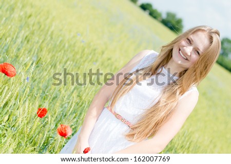 Young beautiful woman happy smiling & looking at camera walking in green wheat field on summer outdoors background