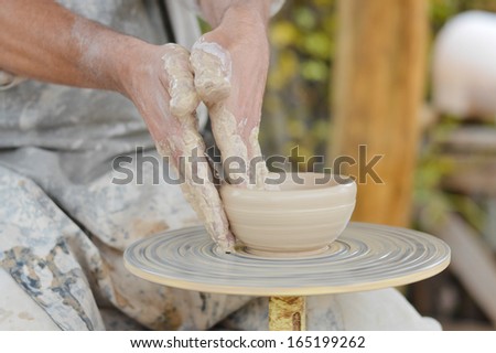 Craftsman making vase from fresh wet clay on pottery wheel hands closeup