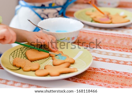 Close up little hands decorating the gingerbread cookies with colorful glaze