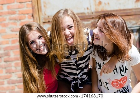 Three young happy smiling & looking at camera teenage girl friends have fun in city outdoors
