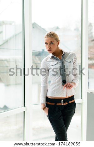 Smiling young business woman standing relaxed near window at her office