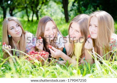 Four beautiful young women girl friends having fun eating strawberries on summer green outdoors background