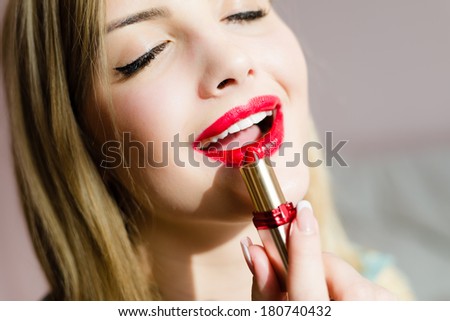 closeup portrait of blonde woman applying red lipstick.