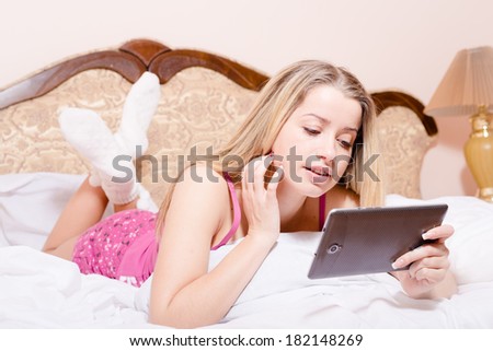 beautiful attractive girl young blond woman in pajamas white socks with tablet pc computer in hands lying talking on skype or taking selfshot or selfy picture of herself on white bed portrait